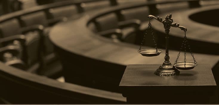 Balança da justiça sobre bancada, numa sala de audiências.